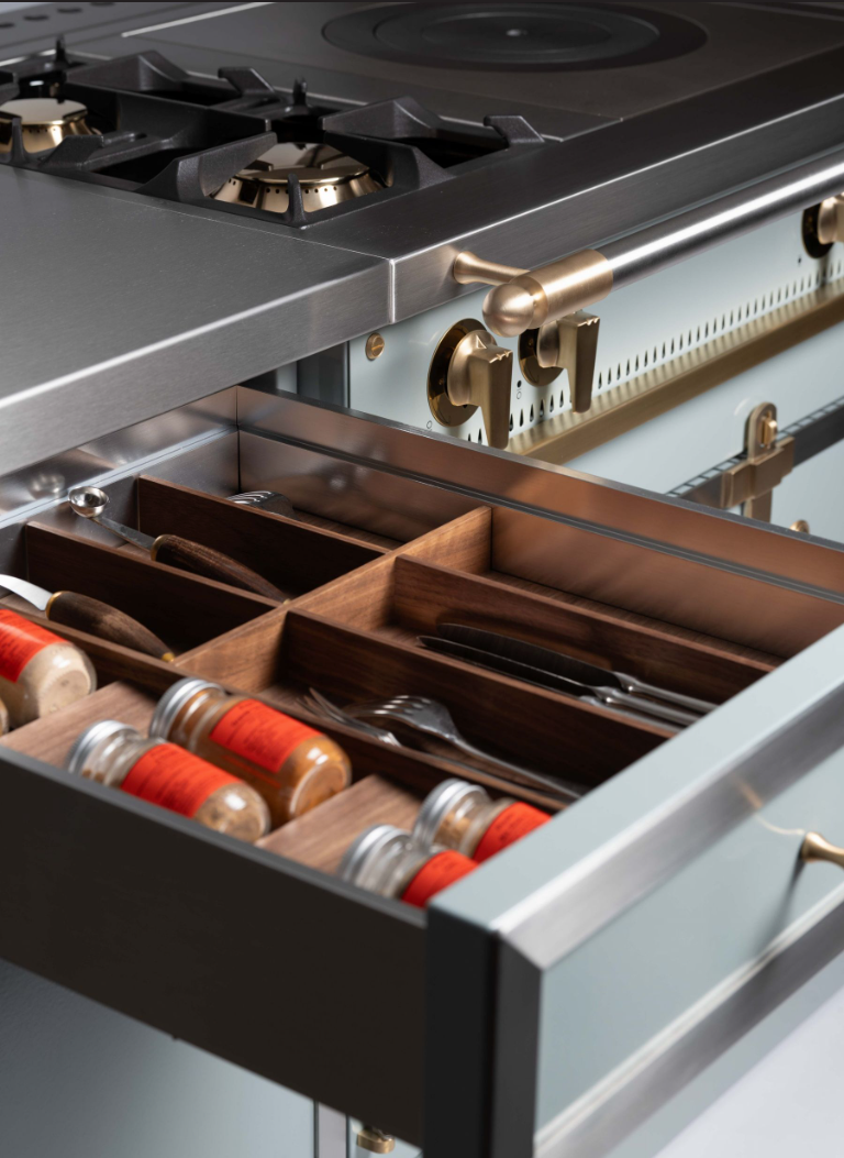 Close-up of a stainless steel kitchen range with an open drawer containing wooden utensil organizers and spice jars with red lids.