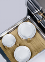 Three white ceramic plates with gold-rimmed edges displayed on a wooden stand inside a stainless steel drawer or cabinet.