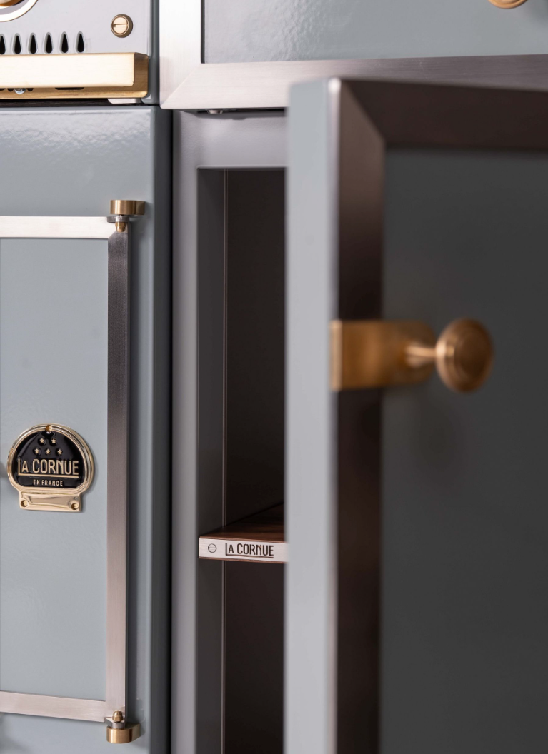 Close-up of a metallic gray Al. Corvique safe with brass handles and a partially open door showing the interior.